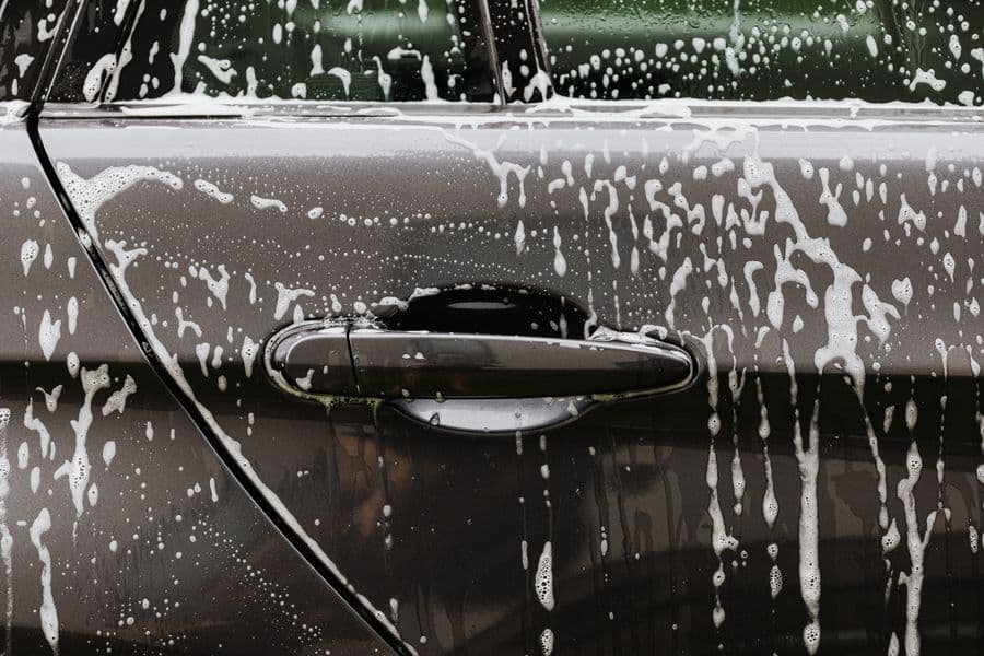 Soap suds sheeting down the door of a dark car mid-wash